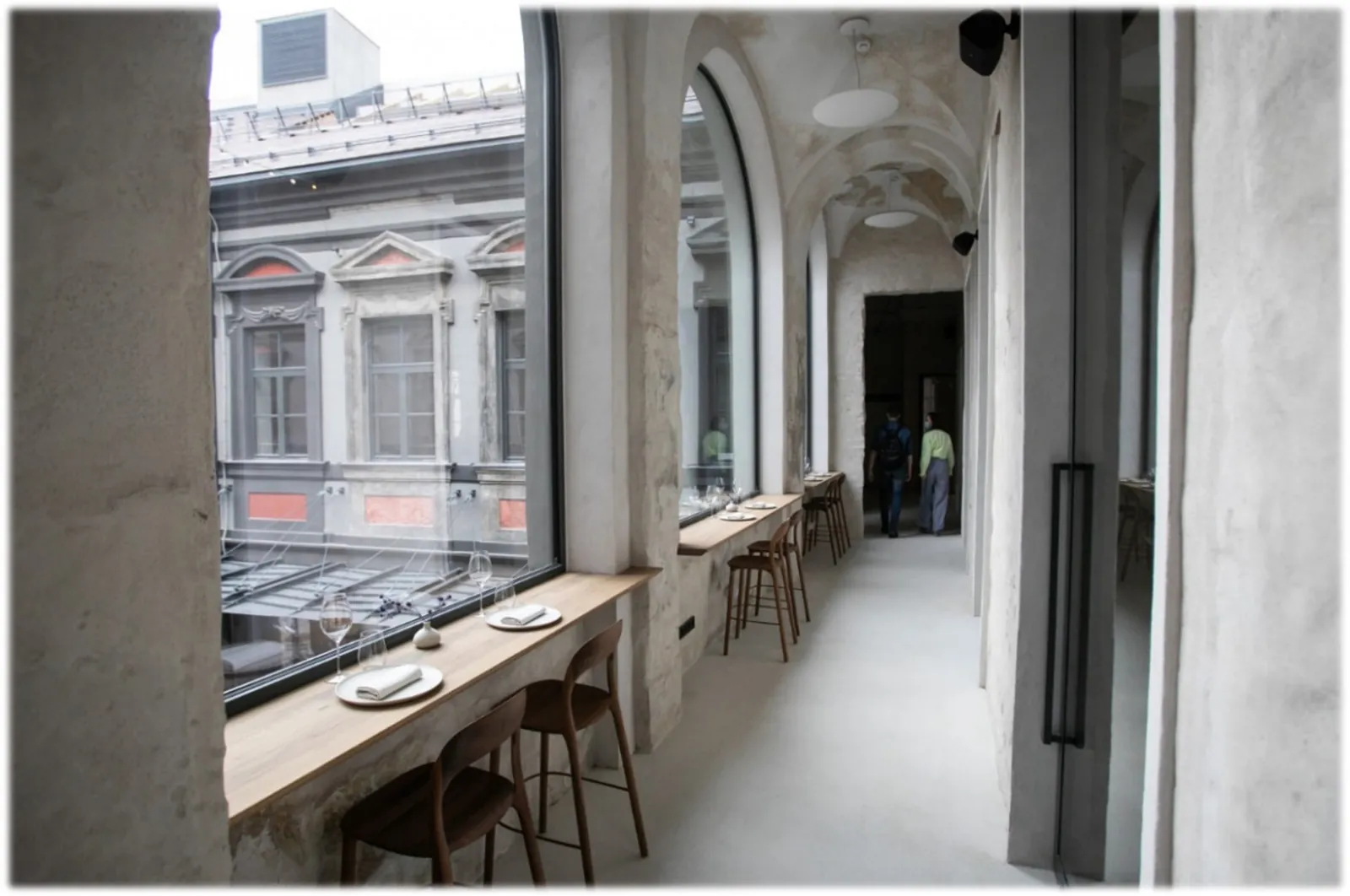 Corridor of a period building lined with tall arched window units looking into a courtyard