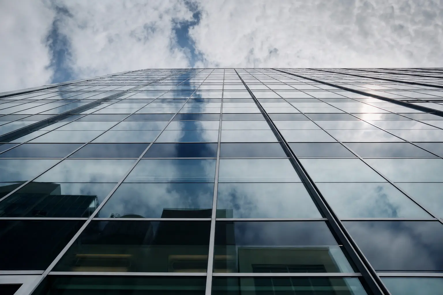 Looking up a curtain-wall elevation, the glass reflecting cloud and sky along the full height