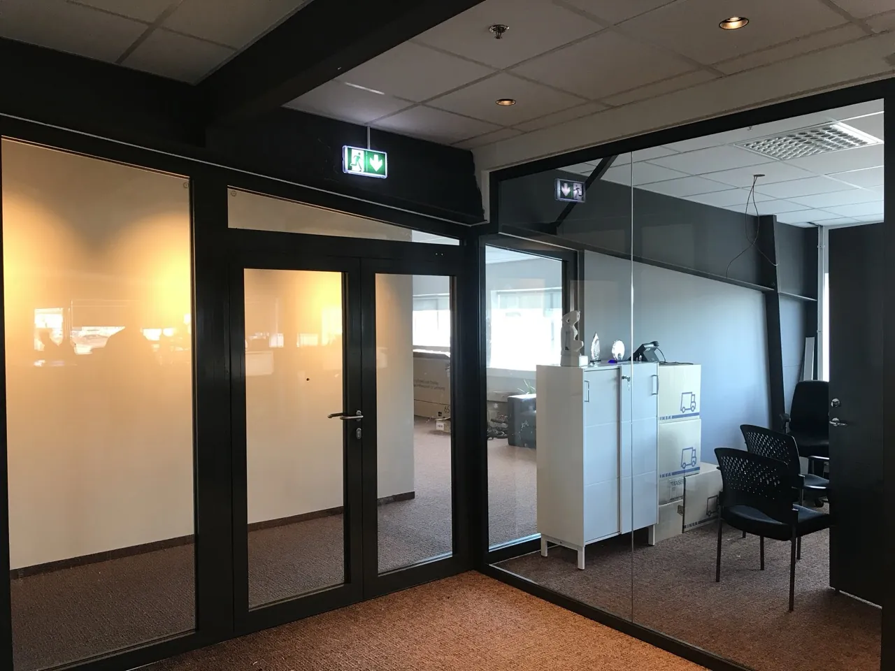 Office interior with dark-framed glazed partition screens and a matching glazed door leaf