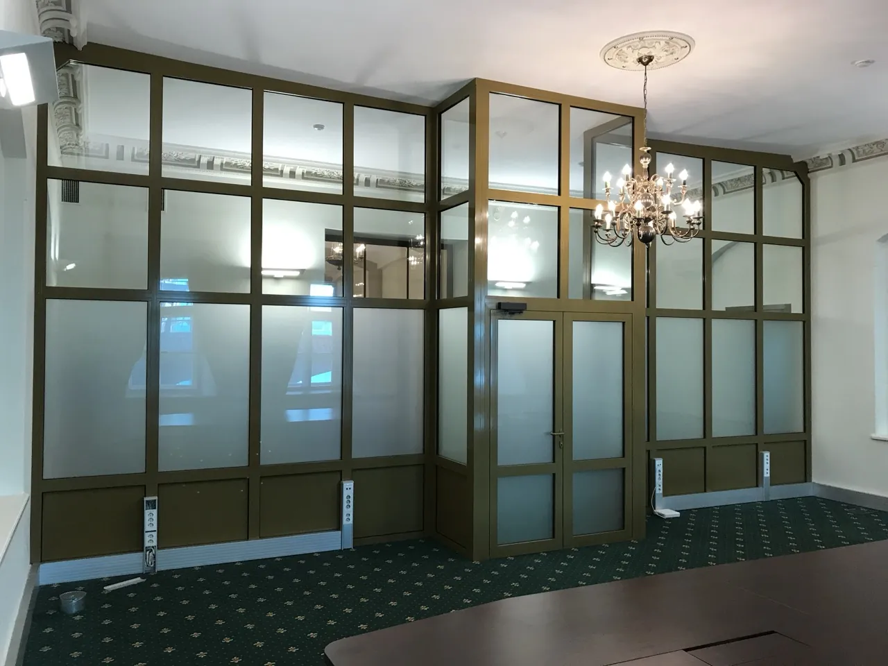 Bronze-framed glazed partition wall dividing a high-ceilinged period room, with a matching glazed door