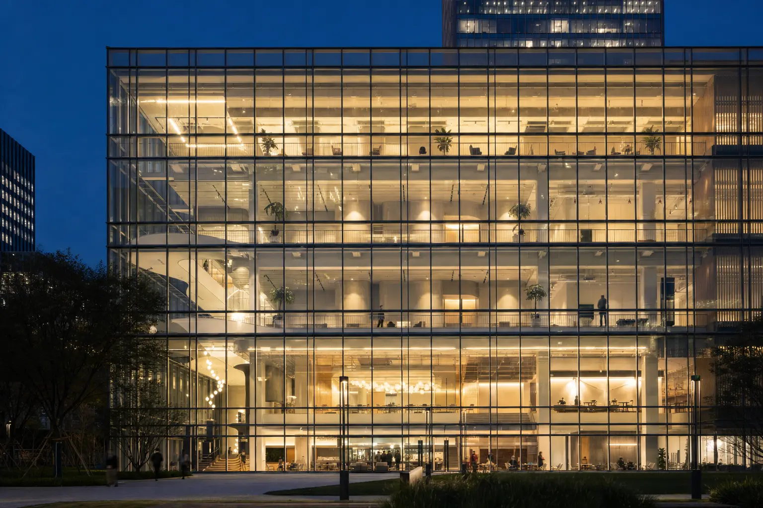 Gridded curtain-wall office elevation at dusk, every floorplate lit from inside behind the glazing