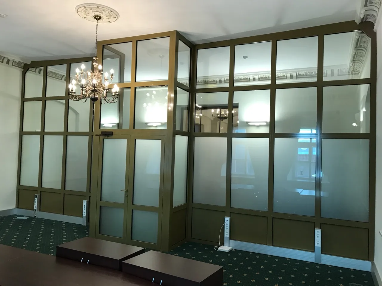 Close view of a bronze-framed glazed partition showing the profile depth, glazing gasket line and door edge