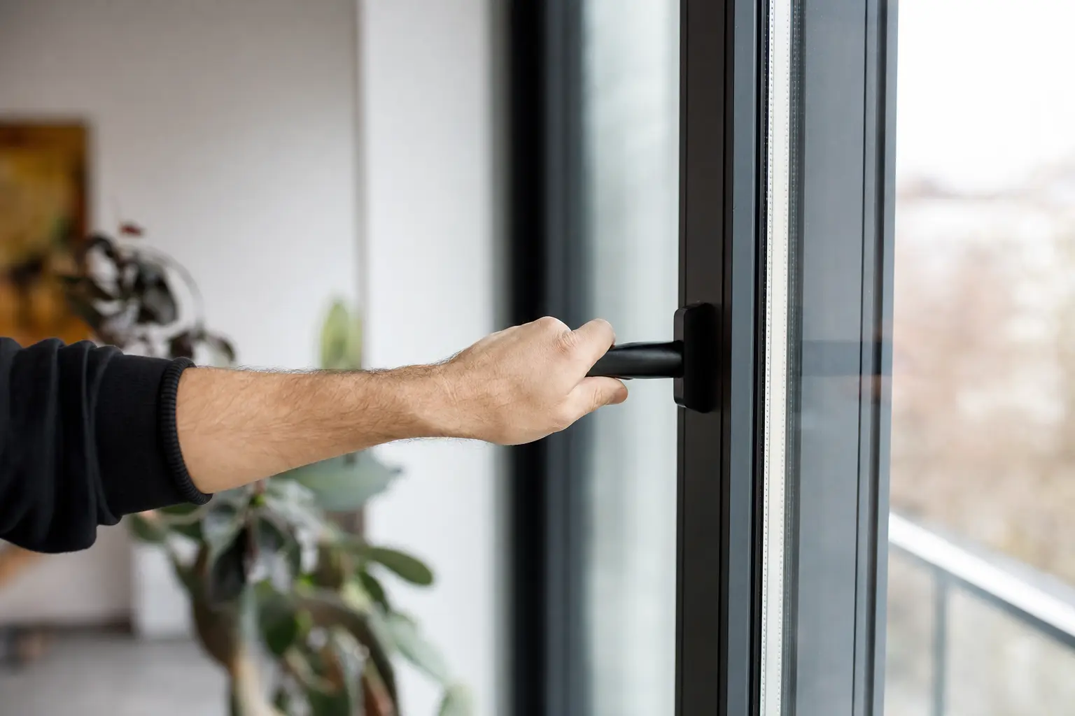 A hand turning the handle on a tall aluminium window in an apartment interior