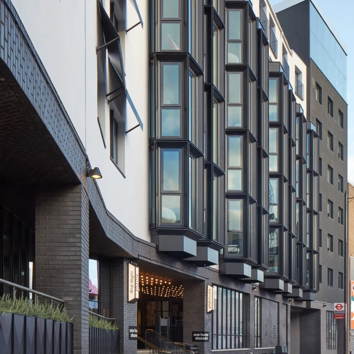 Facade with a grid of projecting black-framed bay window units seen in perspective