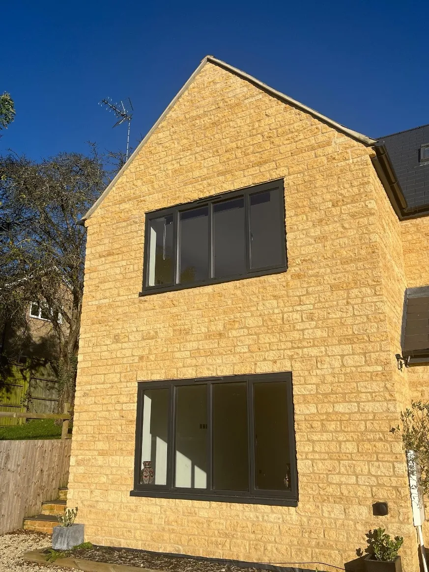 Stone building elevation with two storeys of dark-framed multi-pane glazed doors and windows