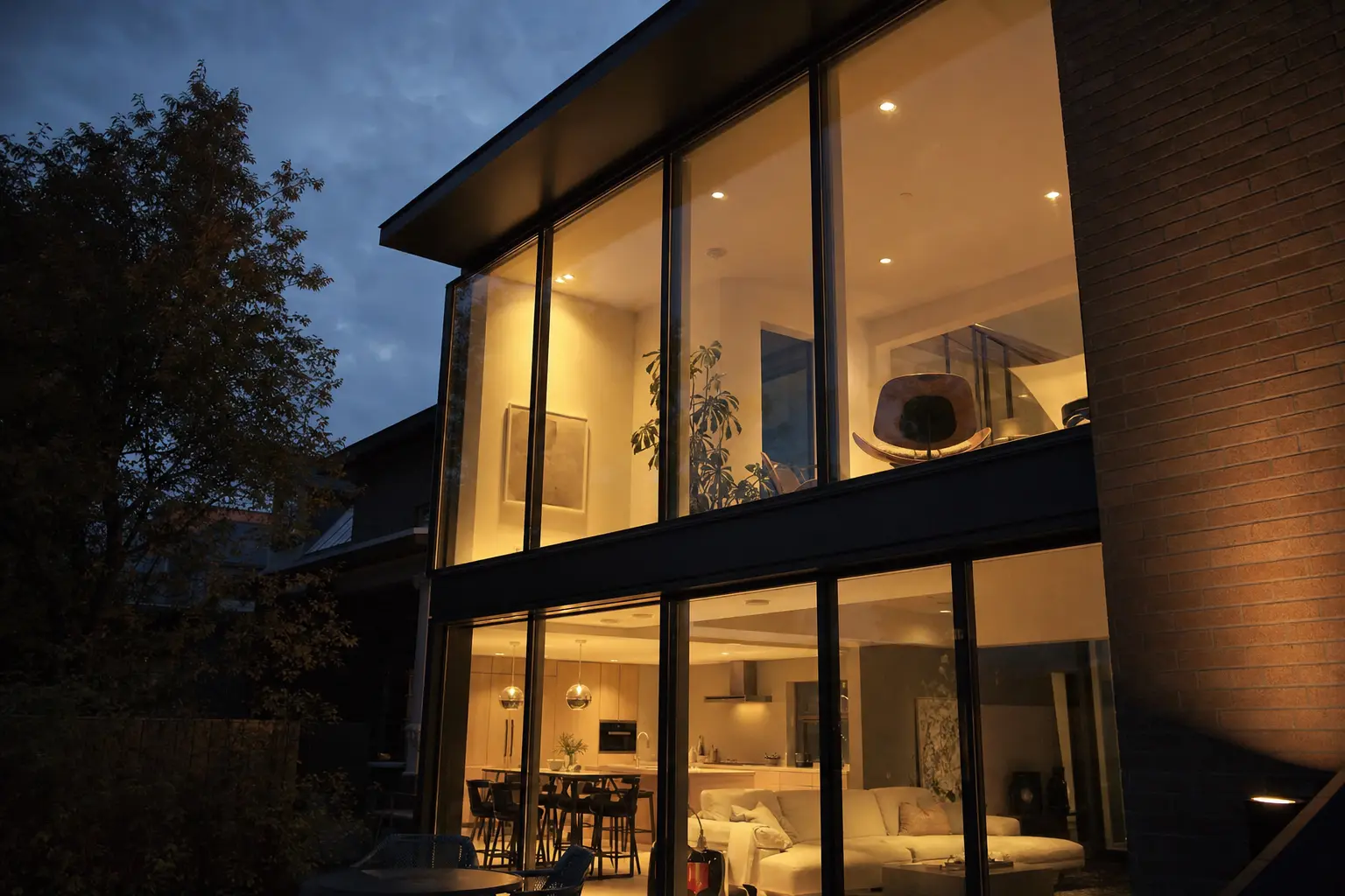 Double-height glazed elevation at dusk, with the lit interior visible through the windows