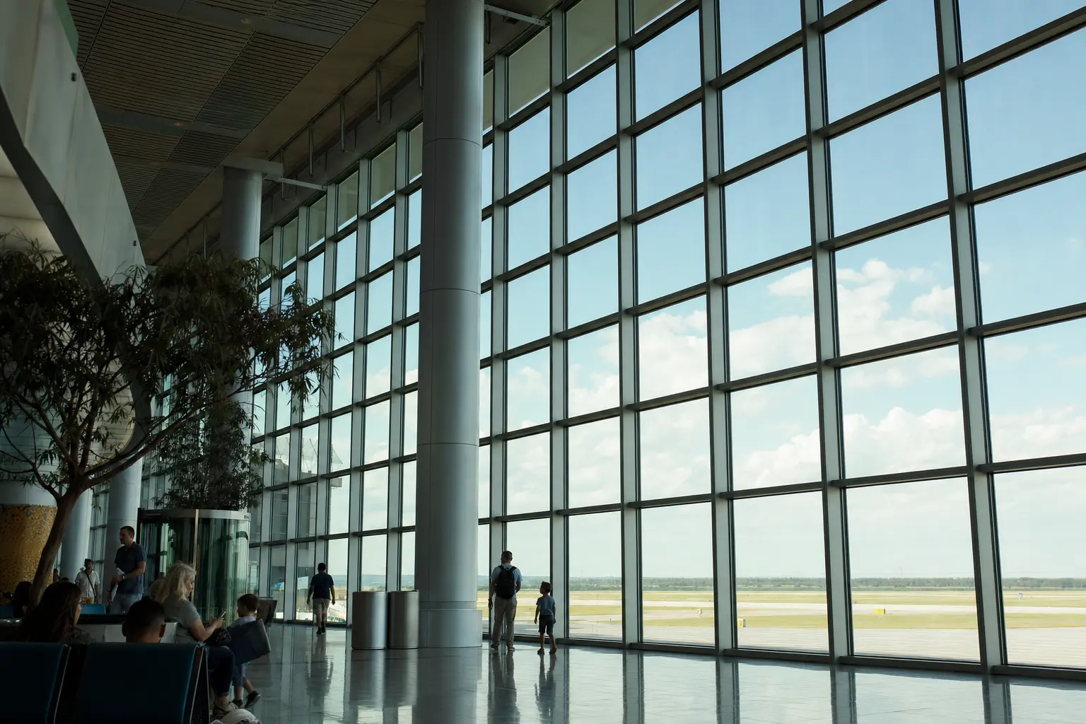 Full-height curtain-wall glazing in an airport concourse, with travellers walking past the mullion grid